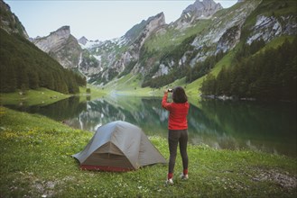 Woman taking photograph by tent near Seealpsee lake in Appenzell Alps, Switzerland