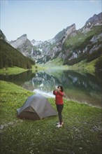 Woman taking photograph by tent near Seealpsee lake in Appenzell Alps, Switzerland