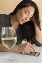 Woman using smart phone next to glass of wine