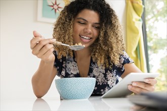 Smiling woman using tablet while eating breakfast