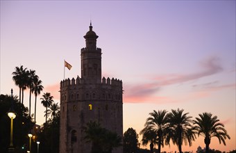 Torre del Oro by palm trees at sunset in Seville, Spain