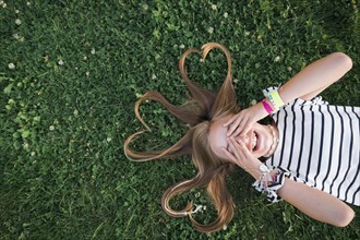 Girl with her hair in heart shapes lying on grass