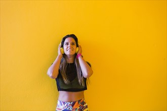 Smiling woman wearing headphones by yellow wall