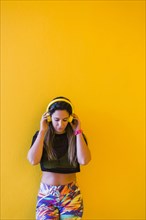 Woman wearing headphones by yellow wall