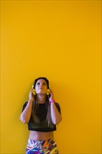 Woman wearing headphones by yellow wall