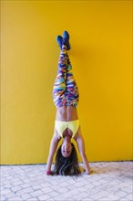Smiling woman doing handstand by yellow wall