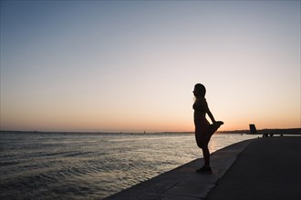 Silhouette of woman stretching at sunset
