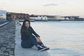 Woman sitting on footpath by sea in Lisbon, Portugal