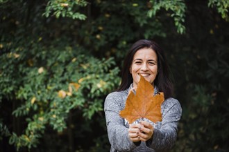 Smiling woman holding autumn leaf