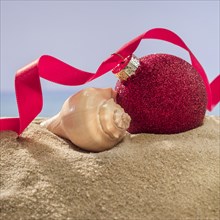 Red bauble and shell on sand