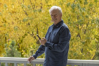 Smiling man holding phone by autumn trees