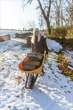 Woman holding wheelbarrow with logs in snow