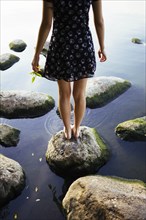 Barefoot woman standing on rock in sea