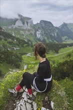 Woman sitting on rock by mountains in Appenzell, Switzerland