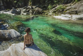 Woman wearing bikini sitting on rock by river