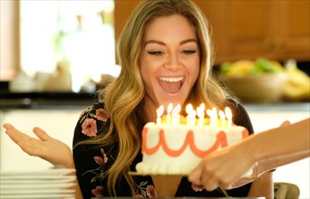 Surprised young woman receiving birthday cake