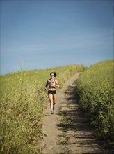 Mid adult woman jogging on path through field