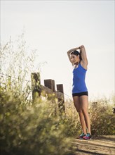 Woman in sportswear stretching by fence