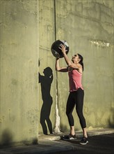 Woman throwing medicine ball against concrete wall