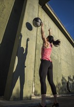 Woman throwing medicine ball against concrete wall