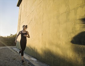 Woman in sportswear jogging by concrete wall
