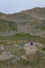 Woman resting on rock by lake while hiking in Herman Gulch, Colorado