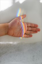 Girl's hand in rainbow light beam in bubble bath
