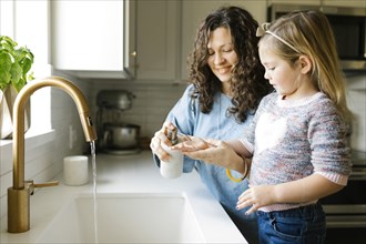 Mother and daughter washing hands in kitchen sink
