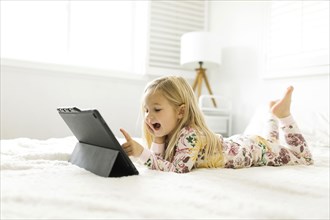 Girl in pajamas using digital tablet while lying on bed
