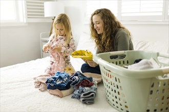 Mother and daughter folding laundry on bed