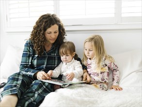 Mother and daughters reading on bed in pajamas