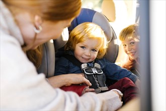 Boy having his seat belt buckled by his mother