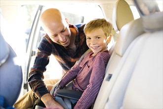 Boy smiling as his father buckles his seat belt