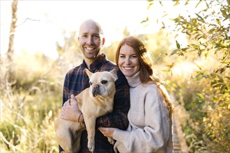 Smiling couple with pet French bulldog in forest