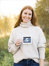 Smiling pregnant woman holding ultrasound photograph