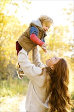 Smiling woman holding her son aloft in forest