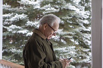 Senior man using smart phone by snowy tree