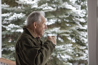 Senior man with cup of coffee by snowy pine tree