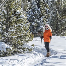 Senior woman in orange jacket with hiking poles in snow