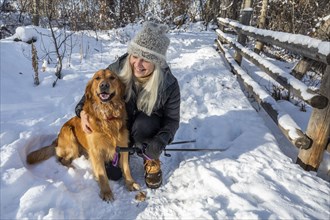 Smiling senior woman petting dog in snow