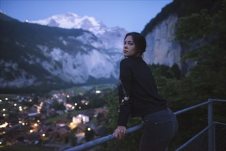 young woman leaning on railing by mountain and village