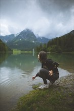 young woman crouching by lake