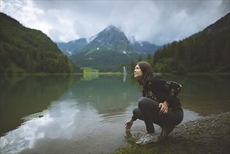 young woman crouching by lake