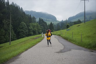 young woman with yellow jacket and backpack walking along country road