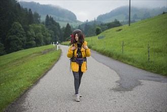 young woman with yellow jacket and backpack walking along country road