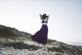 young woman in bra and skirt standing on rock