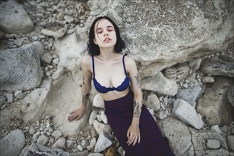 Tattooed woman in blue bra sitting on rocks