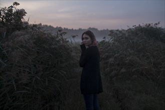 young woman between bushes at sunset