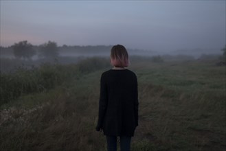 Rear view of young woman in field at sunset