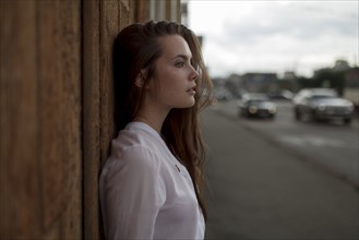 young woman leaning on wooden fence in city